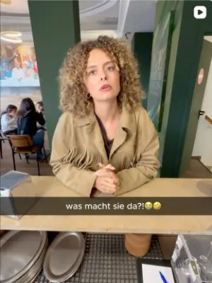 Kundin am Tisch im Laden von Der Eiswerker, Szene aus einem Kurzvideo mit Text „was macht sie da?!“